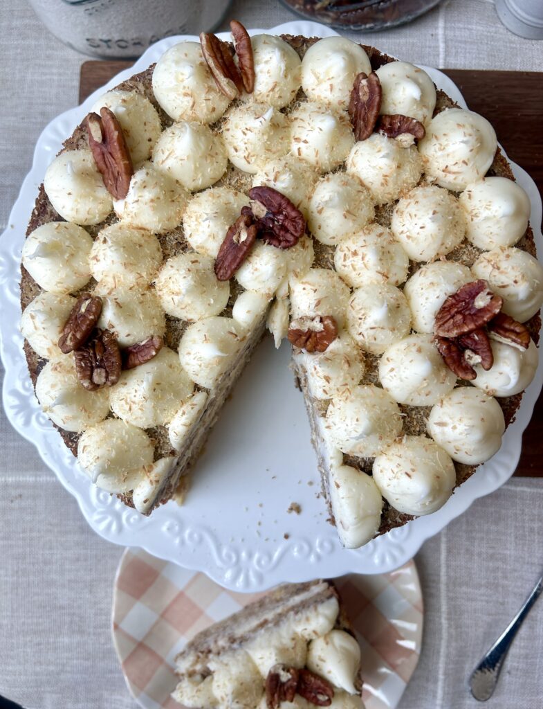 a round cake with cream cheese icing and pecans on top