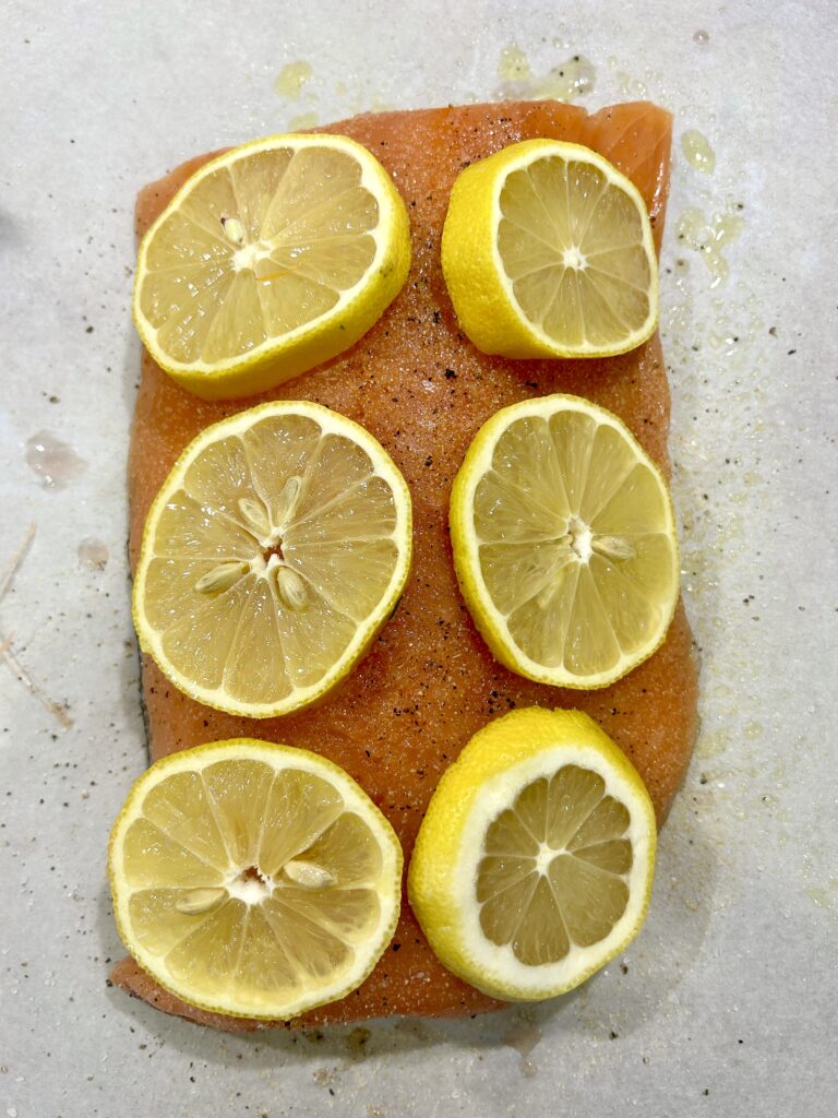 uncooked salmon fillet with lemon slices on top