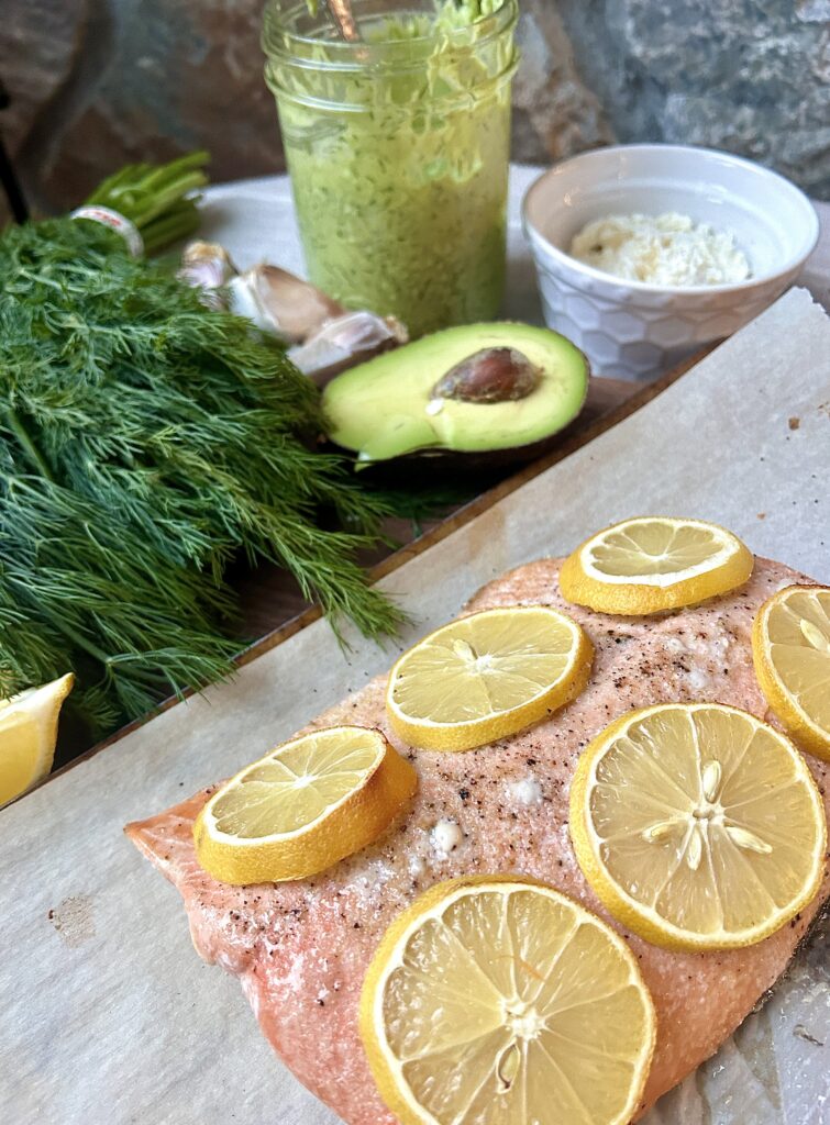 a fillet of salmon on a baking sheet with lemon slices and dill on the side
