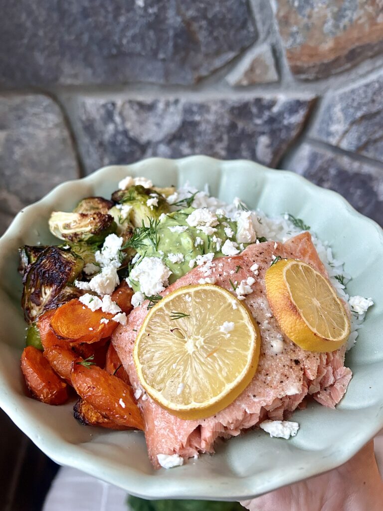 a bowl with rice, carrots, Brussel sprouts and salmon with an avocado sauce
