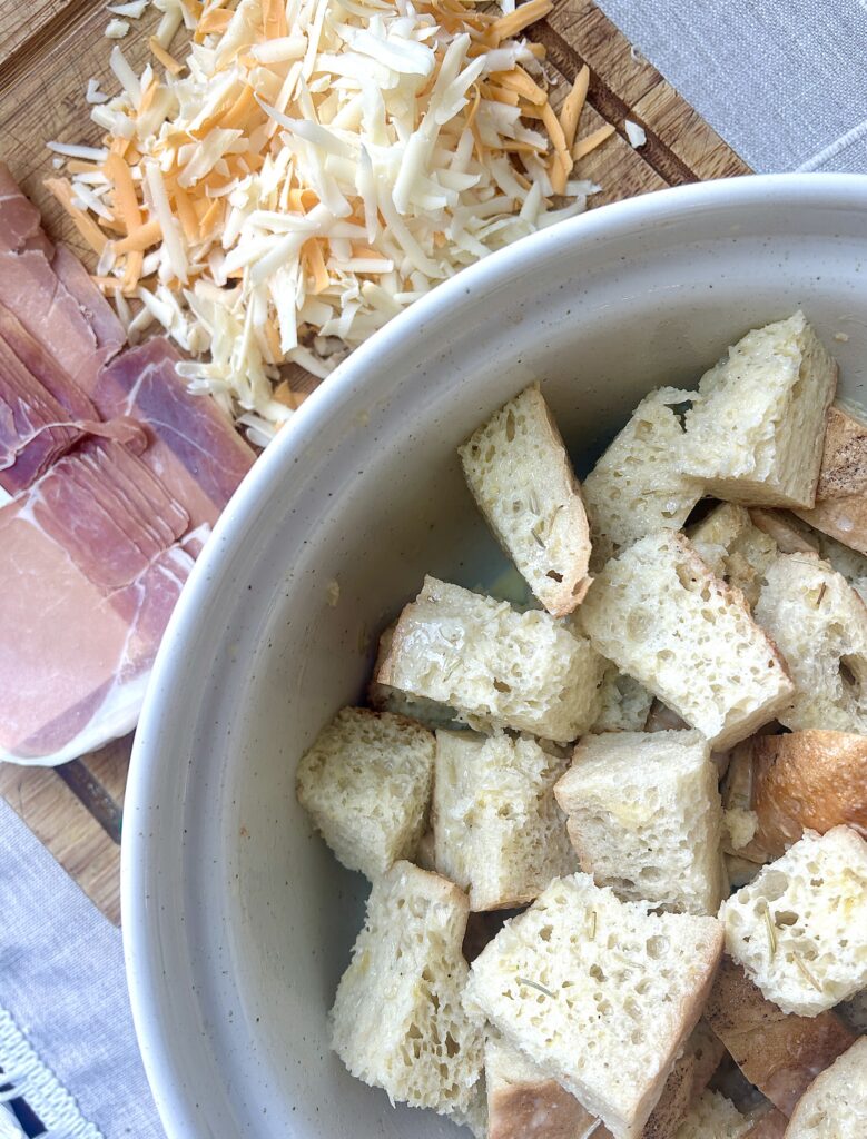 a bowl of cubed bread with cheese and prosciutto on the side