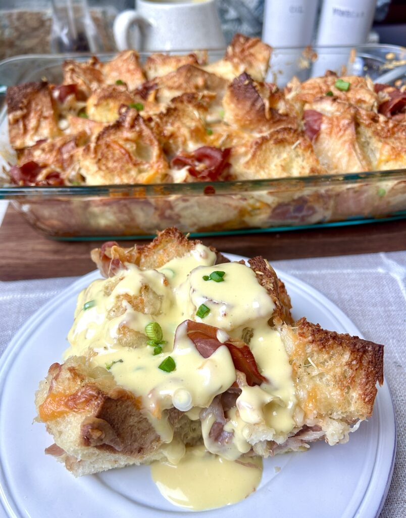 a white plate with a slice of prosciutto, cheese sourdough bake with hollandaise sauce on top