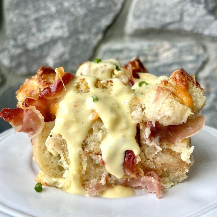 a white plate with cheesy baked sourdough with prosciutto and hollandaise sauce on top