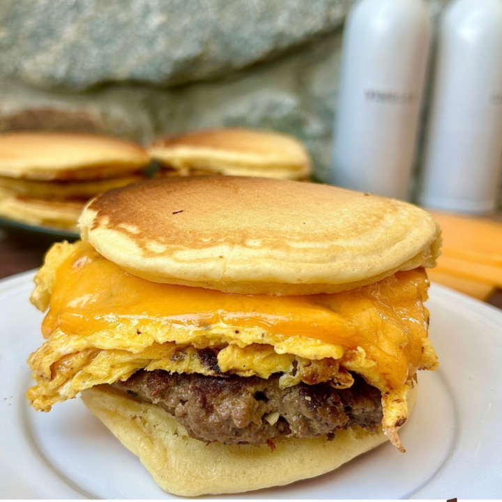 a white plate with a pancake and sausage breakfast sandwich