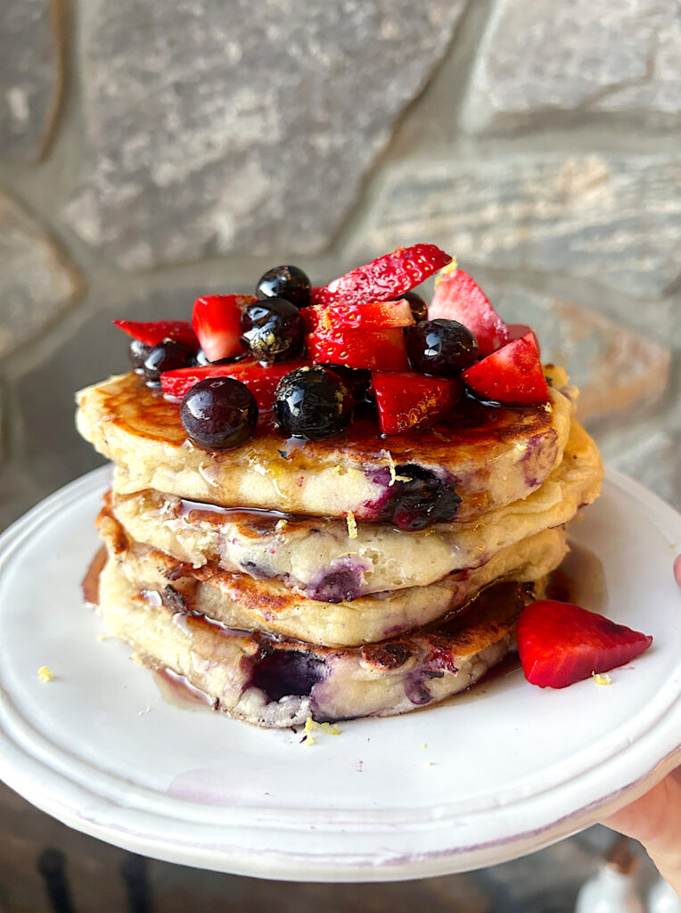 a white plate with a stack of blueberry and strawberry ricotta pancakes