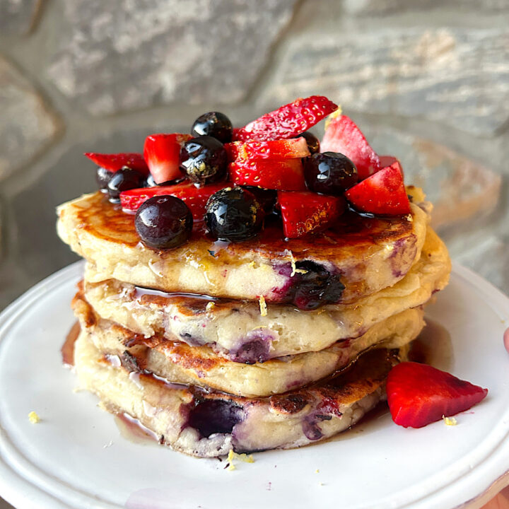 a white plate with a stack of blueberry and strawberry ricotta pancakes