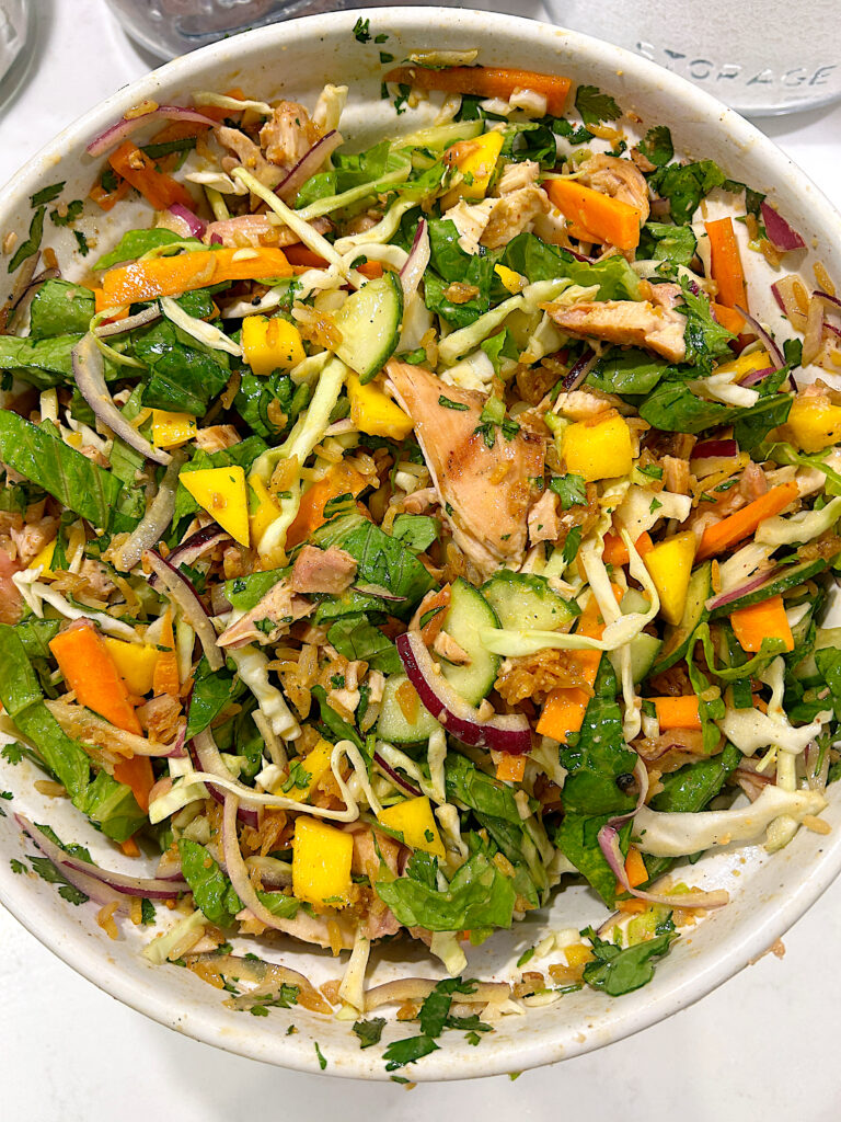 a large bowl of Salad with mango, carrots, cabbage, chicken, crispy rice and a peanut dressing