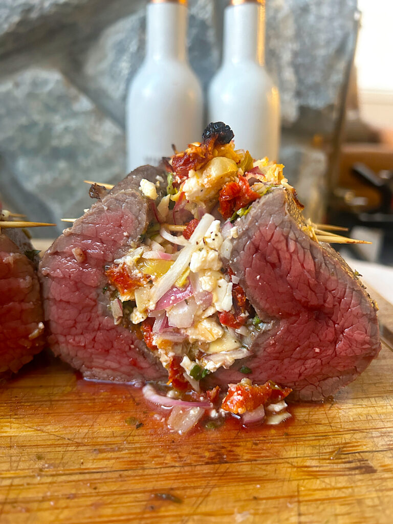 a meat roast sliced in half, stuffed with greek vegetables