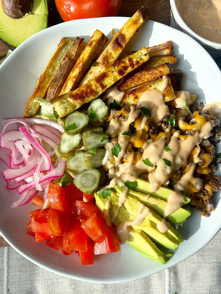 a bowl of ground meat, potato fries, burger toppings and burger sauce