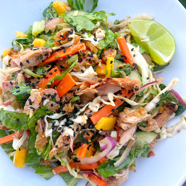 a salad with carrots, cabbage, mango chicken, sesame seeds and a peanut dressing