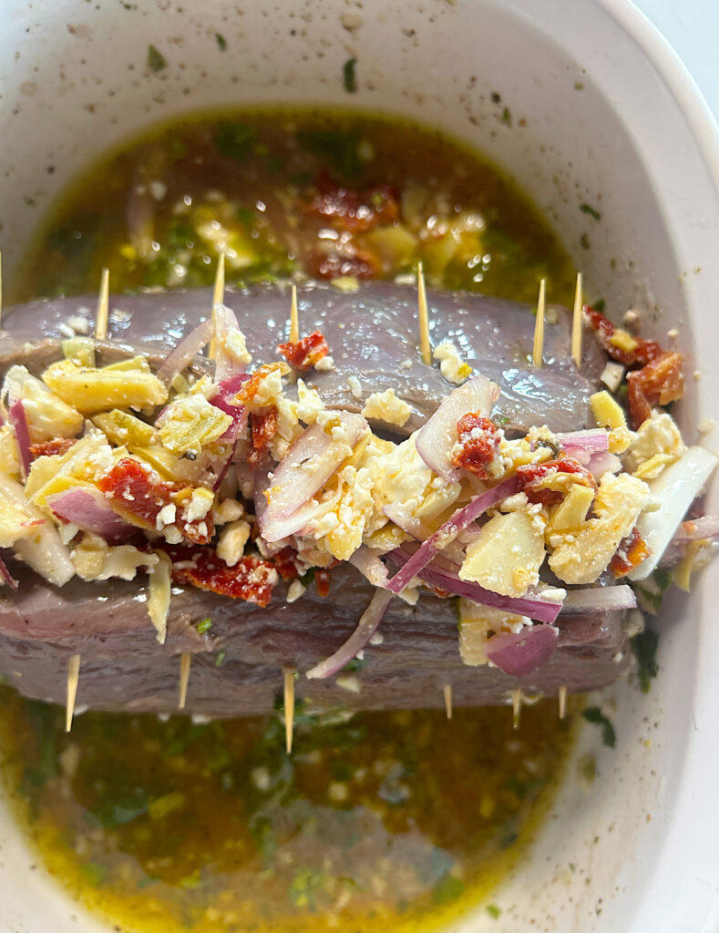 an uncooked roast stuffed with feta cheese, artichokes and sun dried tomatoes