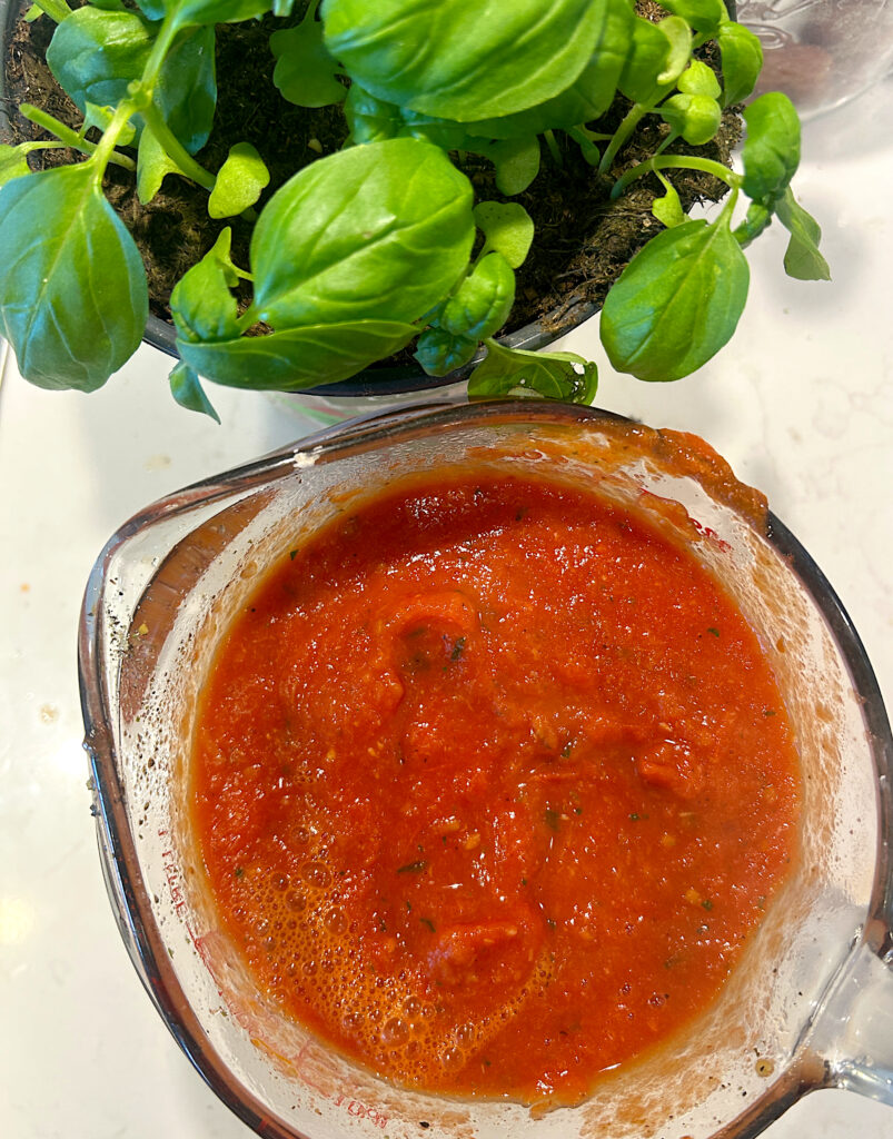 a class measuring cup of tomato sauce with basil