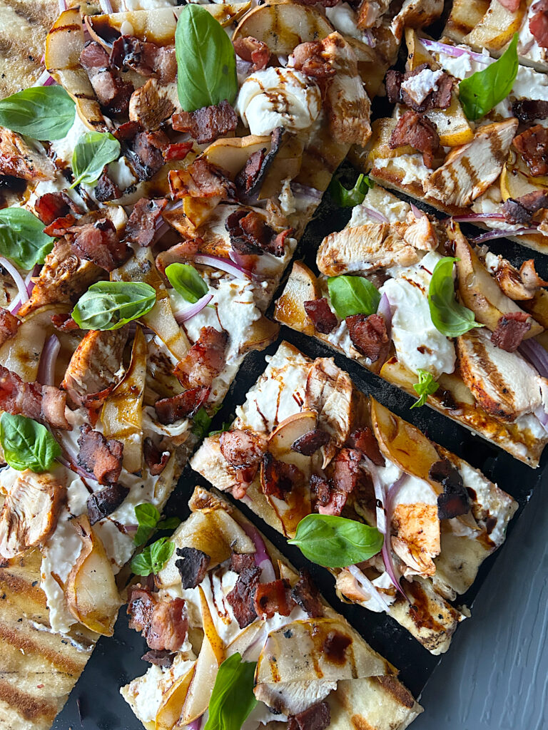 a flatbread with basil, pear, chicken and balsamic glaze sliced into squares