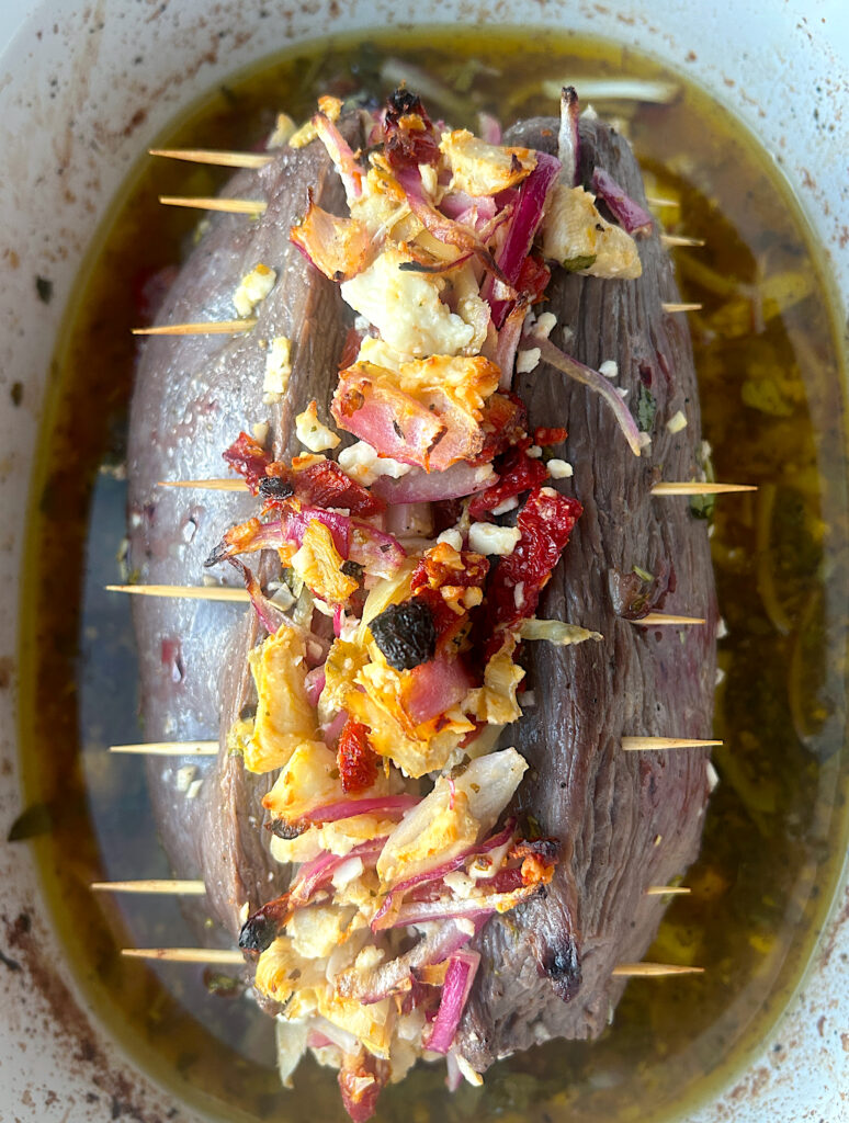 a version roast in a bakin dish, stuffed with tomatoes, artichokes and feta