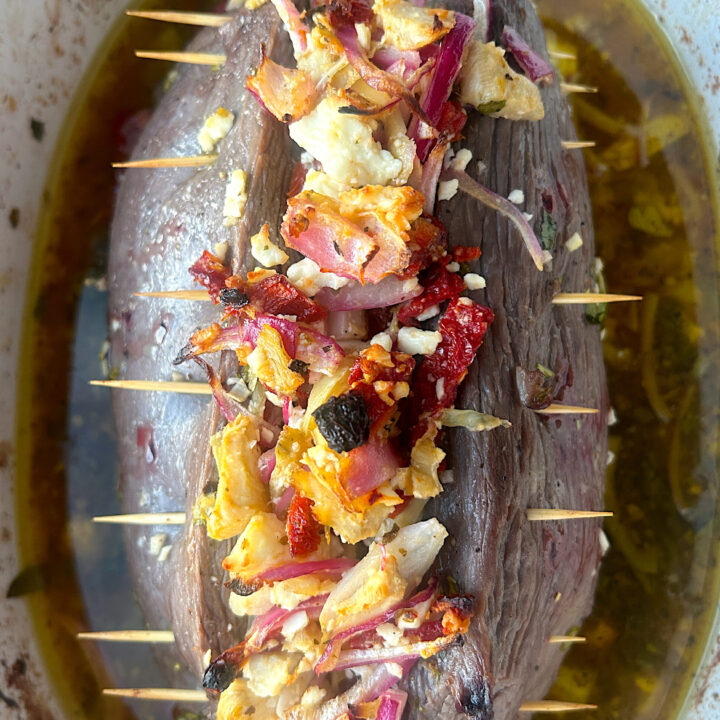 a version roast in a bakin dish, stuffed with tomatoes, artichokes and feta
