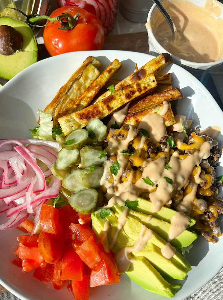 a white bowl with ground meat, cheese, baked fries and burger toppings