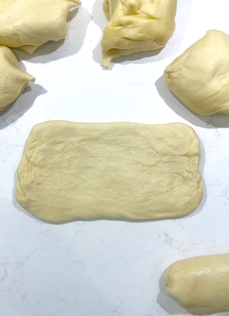 sourdough bun dough stretched into a rectangle on a white counter