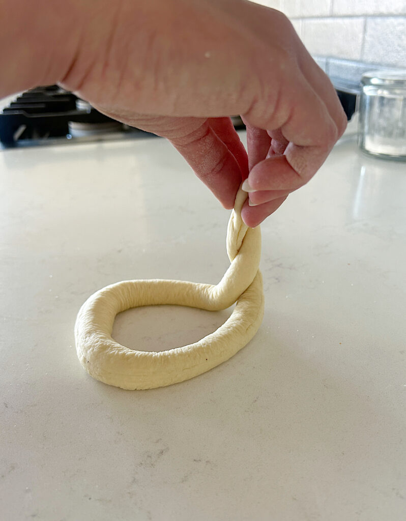 a soft pretzel being shaped by hands
