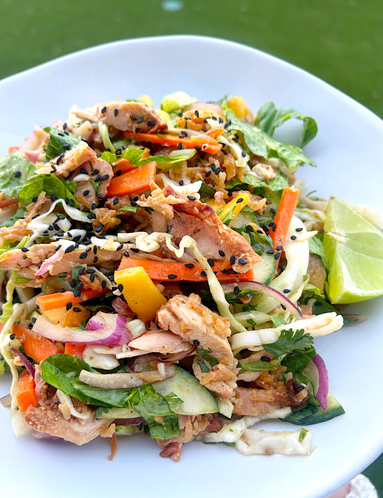 a white bowl of salad with crispy rice, mango, chicken and peanut dressing