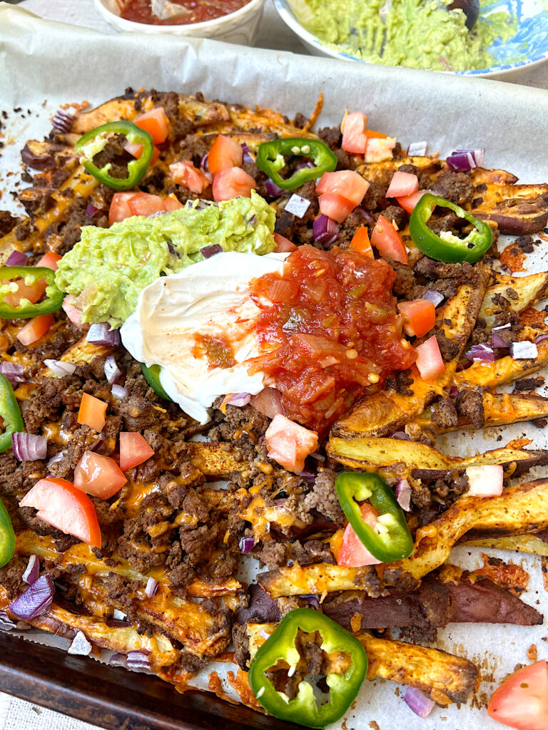 a baking sheet of nachos made with fries, ground venison, sour cream, salsa and guacamole on top