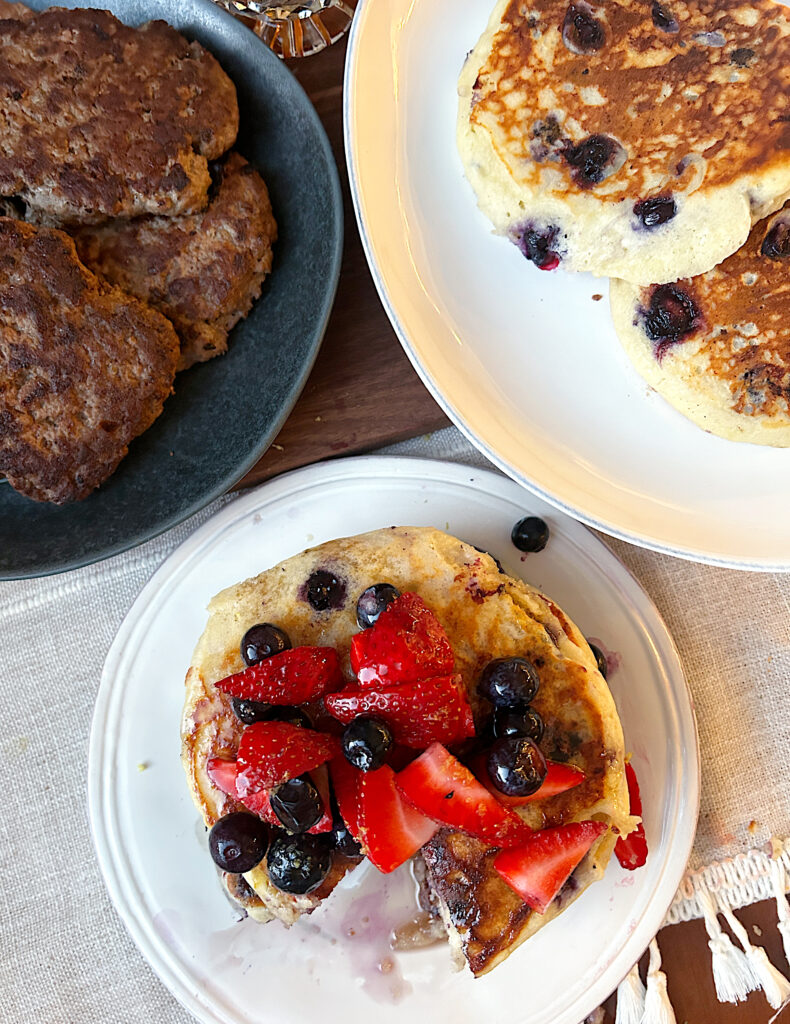a plate of pancakes with berries on top and a plate of sausage patties
