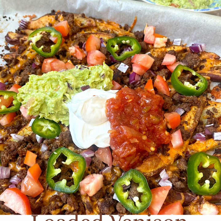 loaded nachos on a baking sheet with ground meat, jalapeños, sour cream, salsa and guacamole