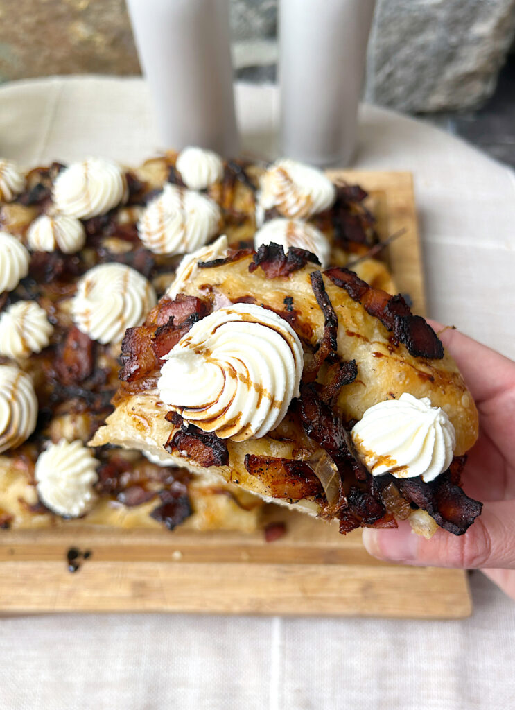 a slice of focaccia bread with bacon, onions and dollops of creamy cheese