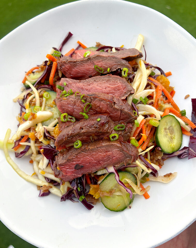 a bowl of salad with crispy rice and sliced steak on top