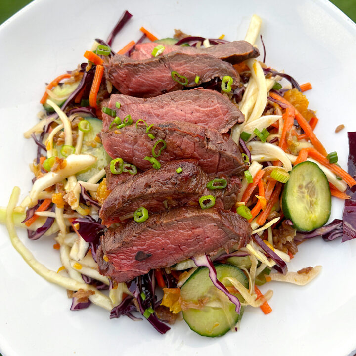 a bowl of salad with crispy rice and sliced steak on top