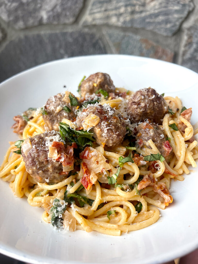 a bowl of spaghetti and meatballs with a cream sun dried tomato and basil sauce