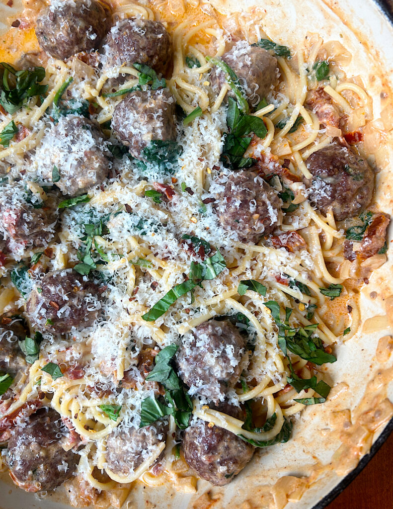 a skillet of creamy sun dried tomato and basil spaghetti with meatballs