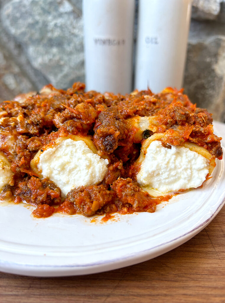 a white plate with ricotta stuffed pasta and a meaty red sauce