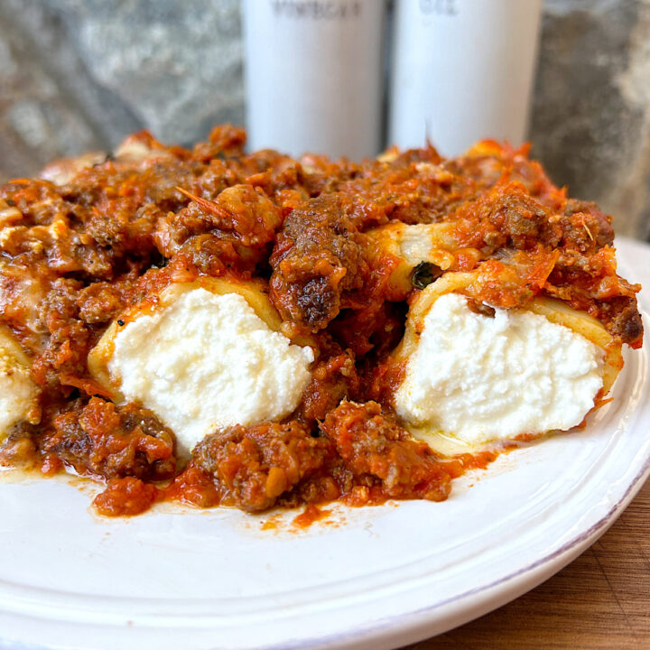 a white plate with ricotta stuffed pasta and a meaty red sauce