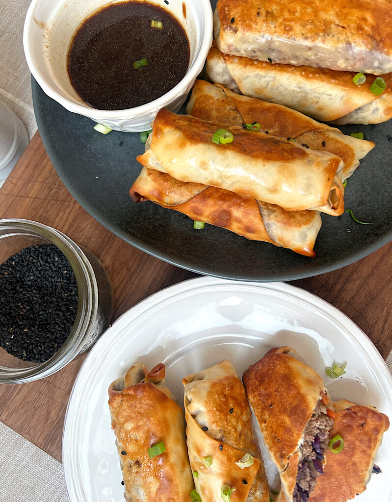 a black plate with golden egg rolls and dipping sauce