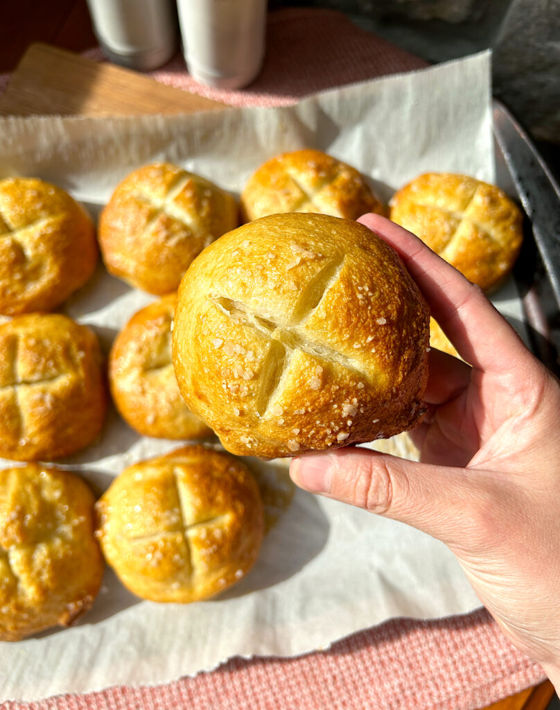 a golden pretzel buns with a cross cut into it and sea salt on top