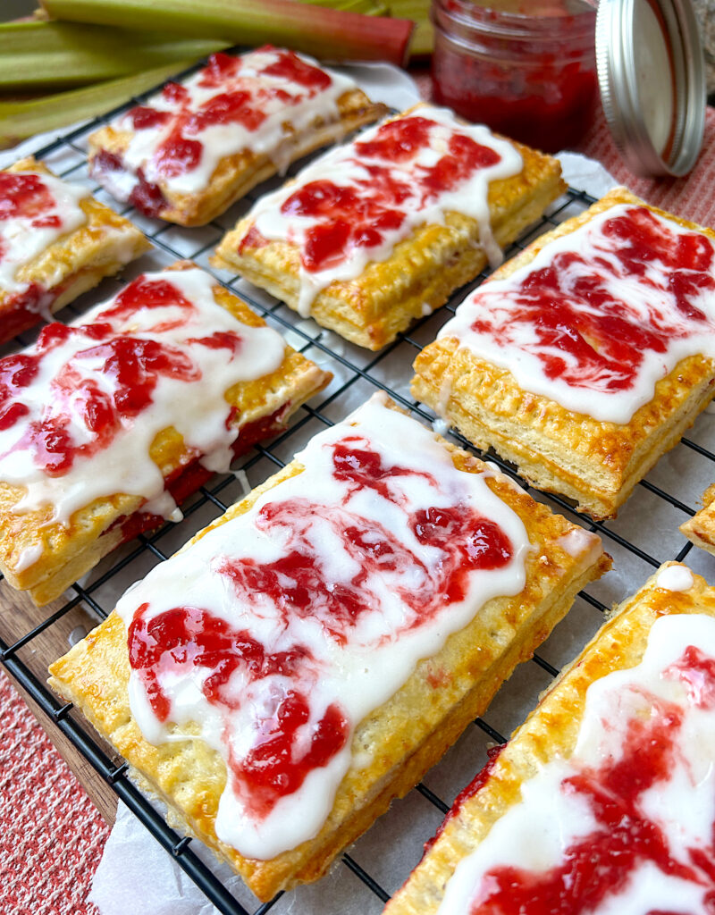 a wire rack full of strawberry rhubarb hand pies with vanilla and strawberry swirl icing