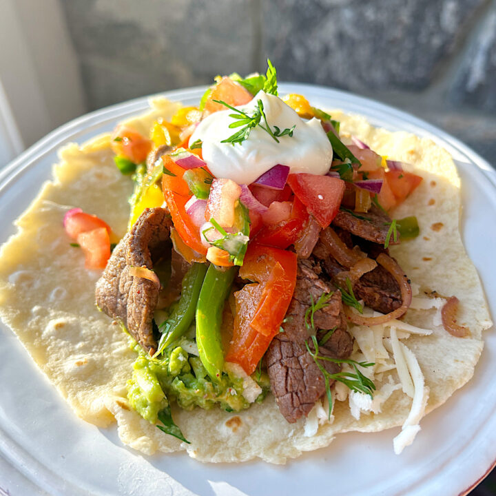 a soft tortilla filled with sliced steak, peppers, onions, pico de Gallo and sour cream