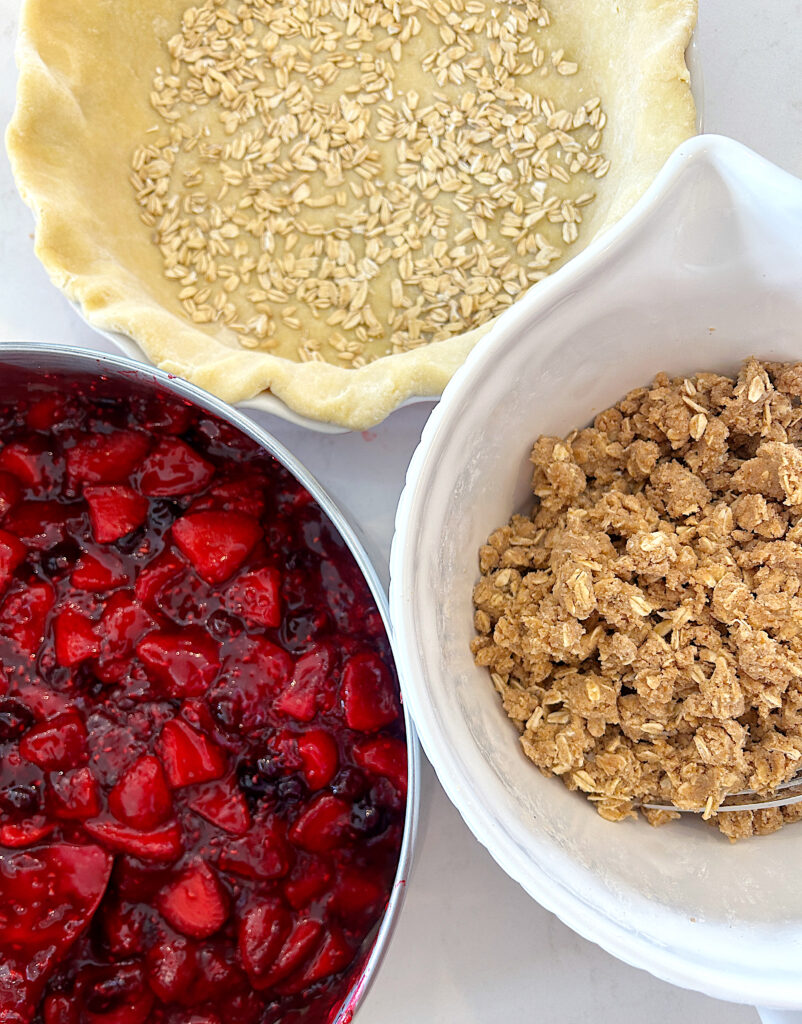 an unbaked pie crust, berry pie filling and crumble topping on a white counter