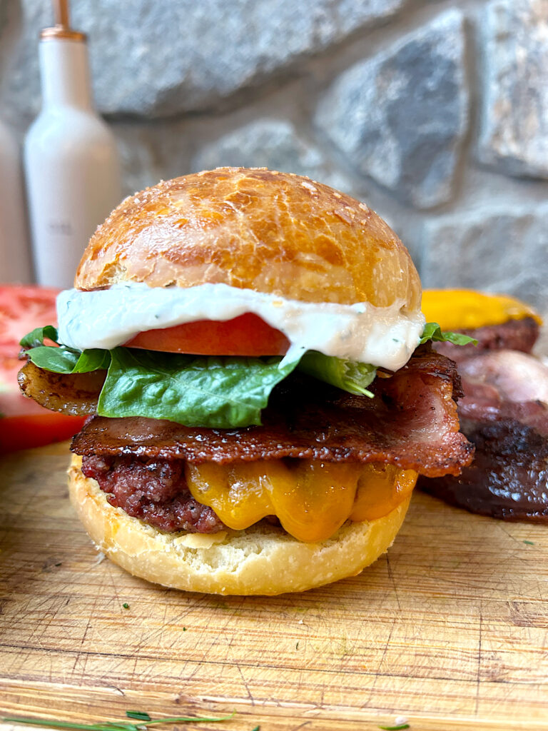 a cheese burger ibuprofen a wood board with bacon, lettuce, tomato and ranch sauce