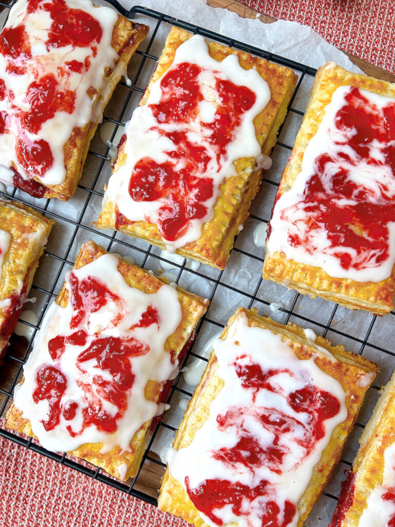 a baking rack of hand pies with strawberry rhubarb filling and vanilla icing
