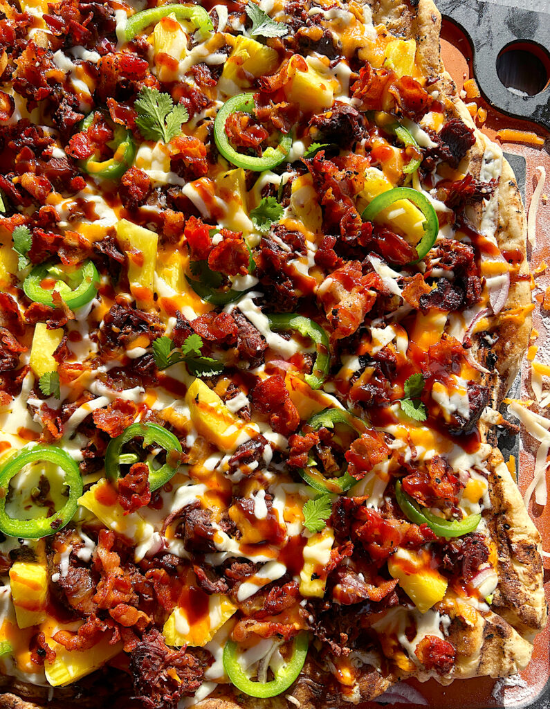 a flatbread pizza with bbq venison, pineapple, cheese, and jalapeños