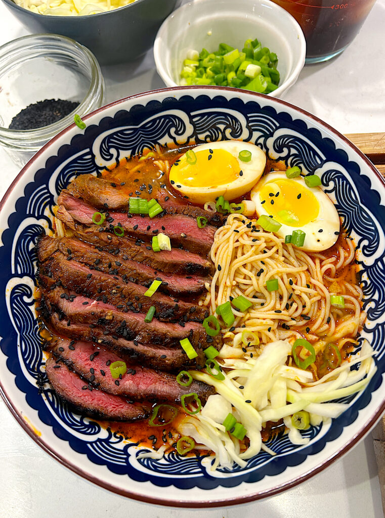 a bowl of steak ramen with cabbages, green onion and a soft boiled egg
