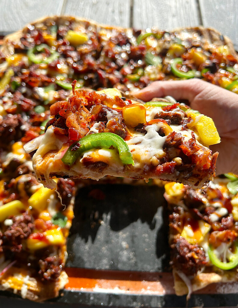 a slice of bbq flatbread pizza with pineapples, meat and bacon