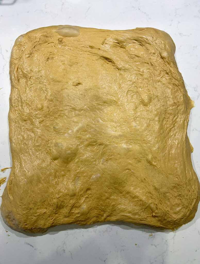 bread dough stretched into a rectangle on a white counter