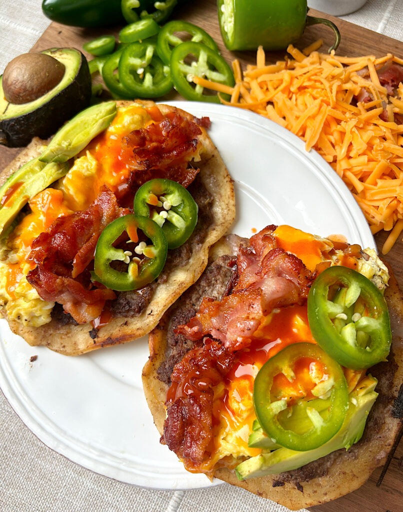 a white plate with two soft tacos with bacon, eggs, sausage and jalapeƱos