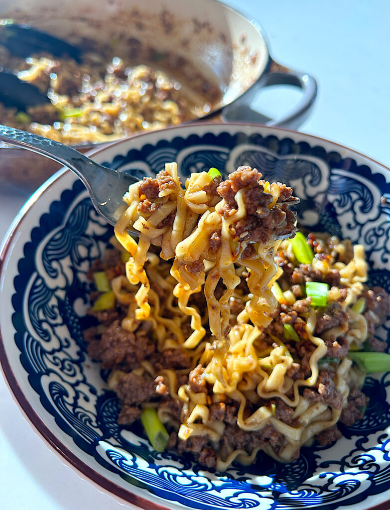 a blue and white bowl of ramen noodles with mongolian sauce and ground venison