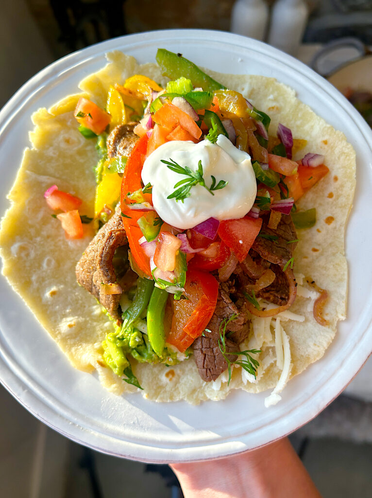 a soft tortilla with peppers, onion, steak strips, sour cream and salsa