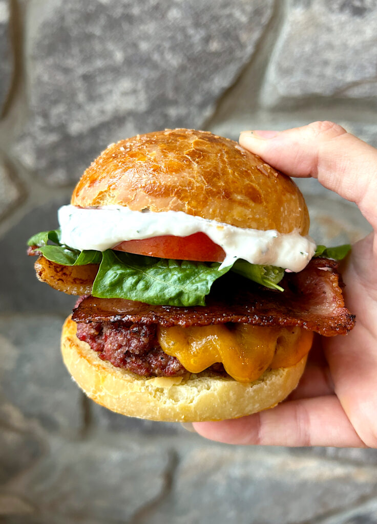 a brioche bun with beef patty, cheese, tomato, lettuce and bacon