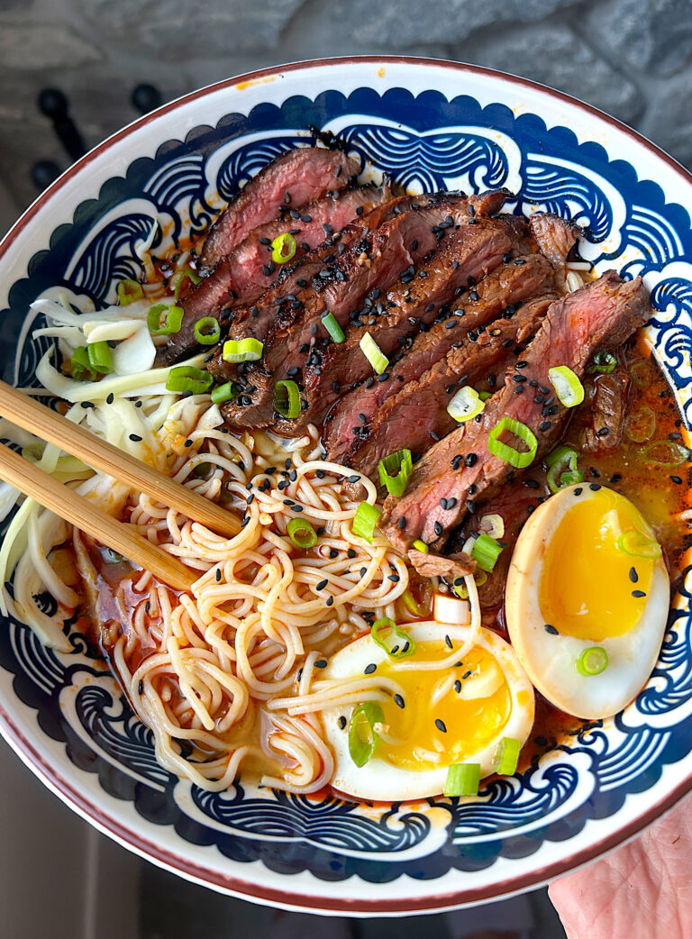 a blue and white bowl of ramen noodles with sliced steak and a boiled egg