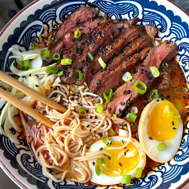 a blue and white bowl of ramen noodles with sliced steak and a boiled egg